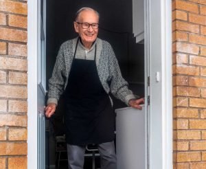 Elderly man looking out at people outside his door