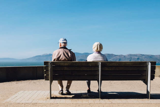 old couple sitting on a bench looking at mountains