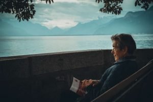 elderly man sitting on bench holding a book