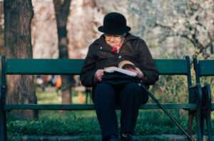 elderly woman sitting on a bench in a park reading a book